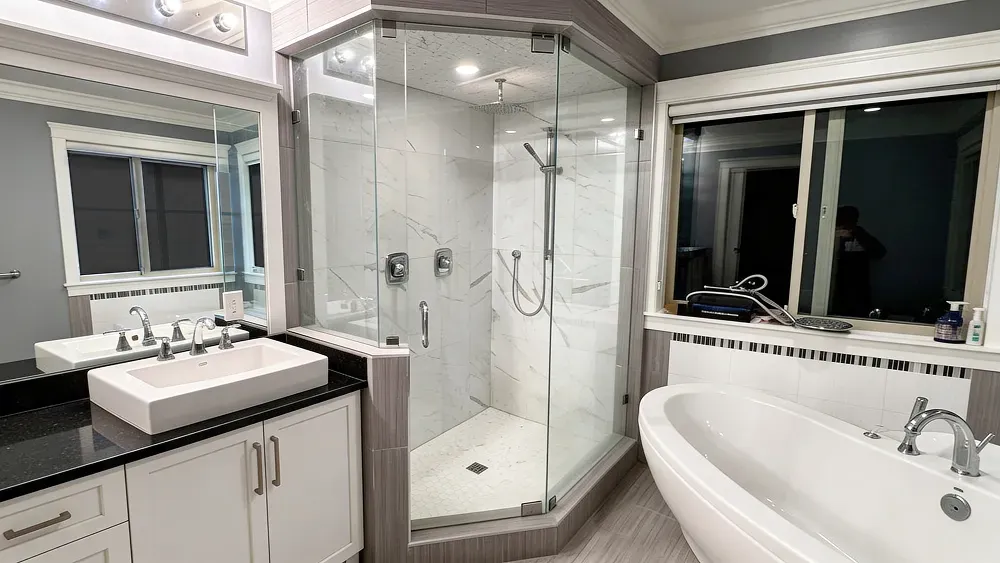 Wide-angle shot of a bright, modern bathroom remodel showcasing new white cabinetry, tiled shower, and updated lighting by PCC.