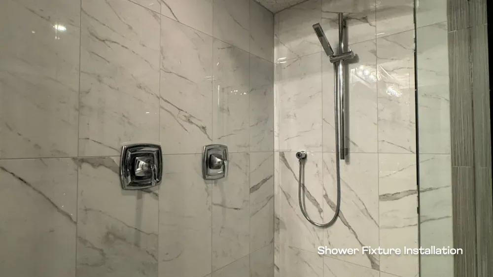 Close-up of chrome shower fixtures and marble-patterned tile work in a Port Coquitlam bathroom renovation by PCC Renovations